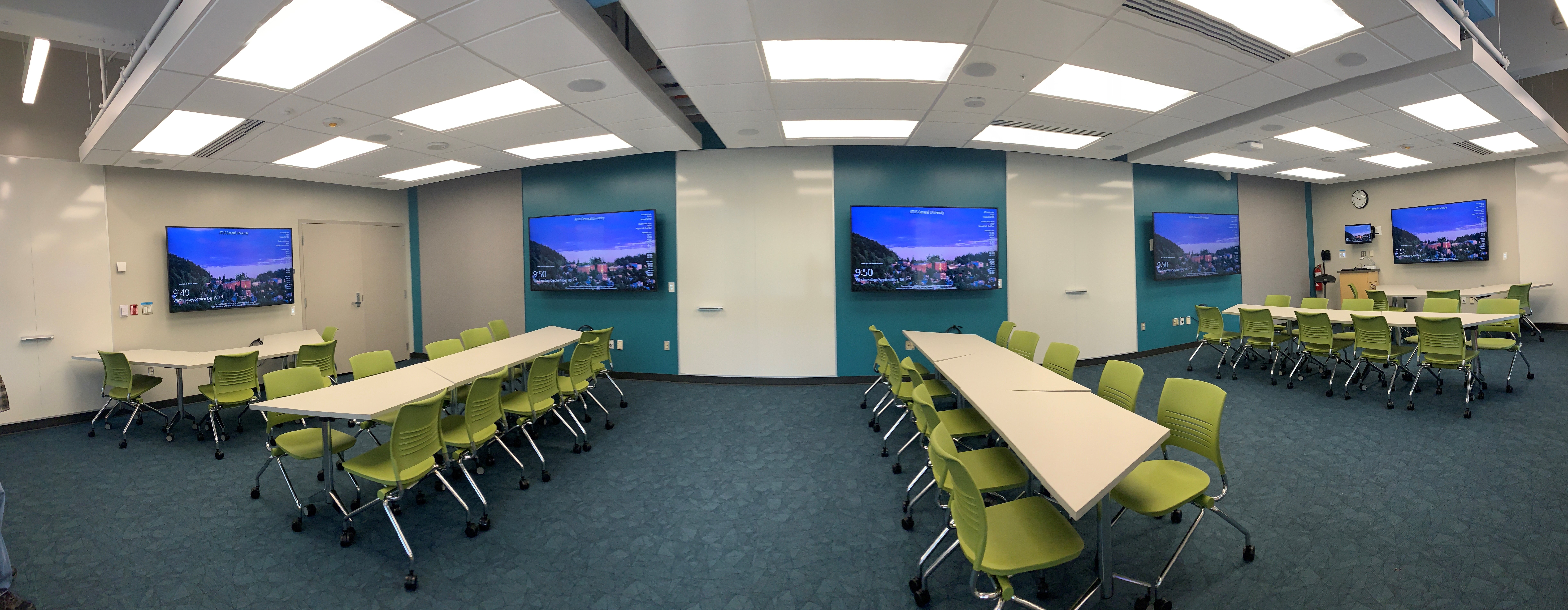 Panoramic view of the room consists of carpet floors, moveable and arrangeable tables and chairs, five TV monitors spread out around the room for different, collaborative viewing options.