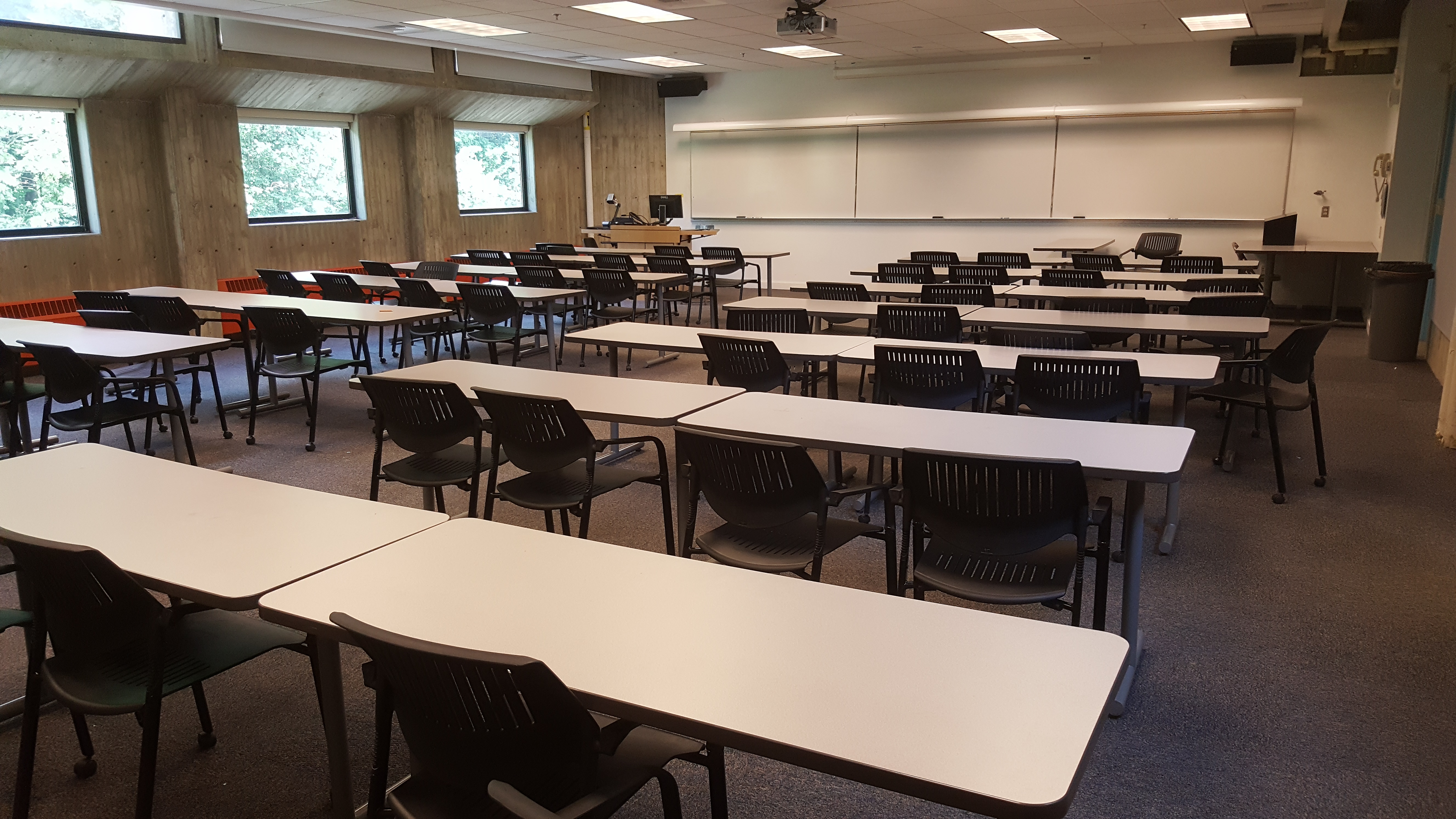 Room Consists of hard floors, moveable tables and chairs, a white board and podium are both located at the front of the room.