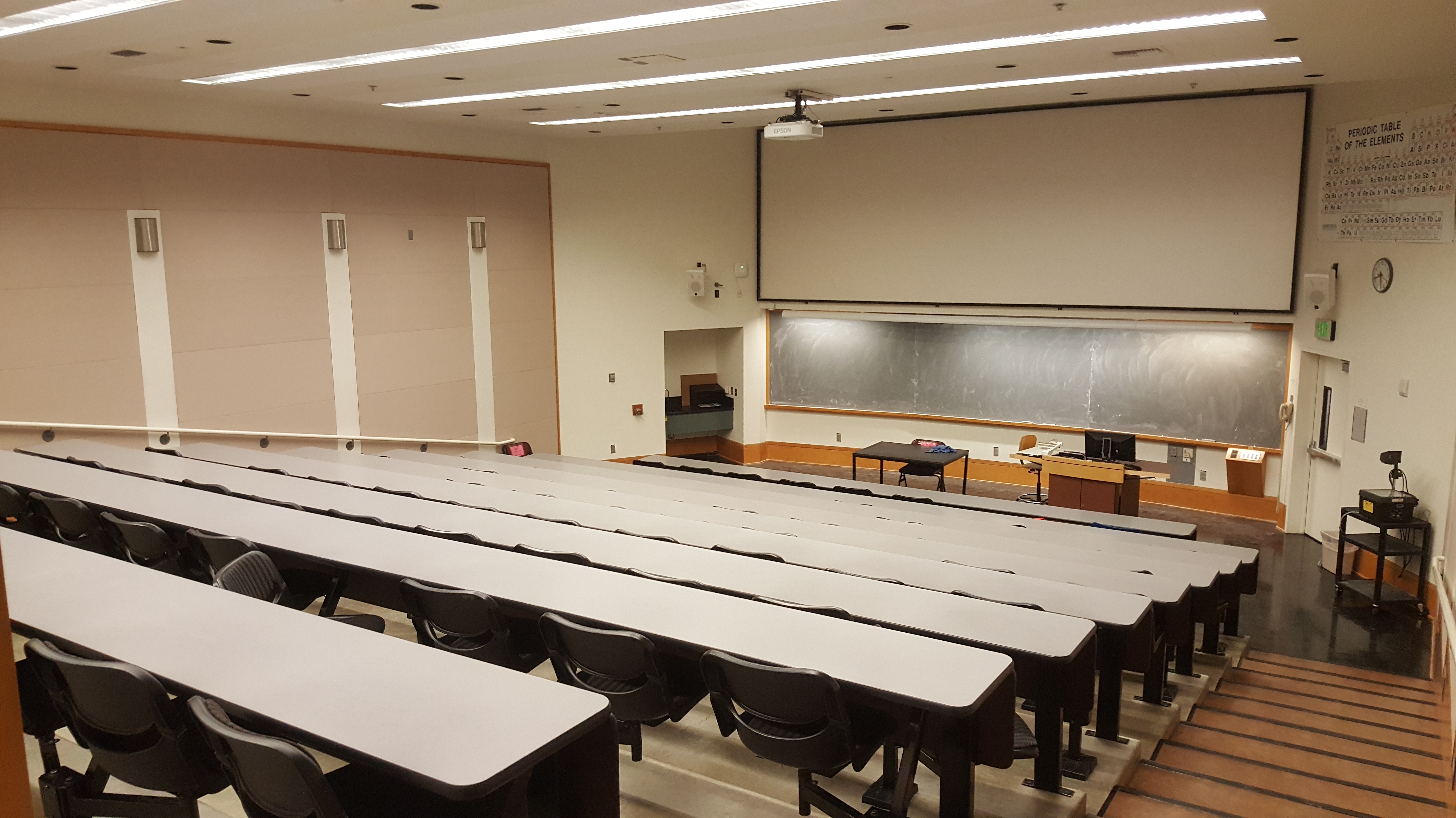 Room Consists of auditorium style, stationary tables and chairs, White board and podium are located at the front of the room.