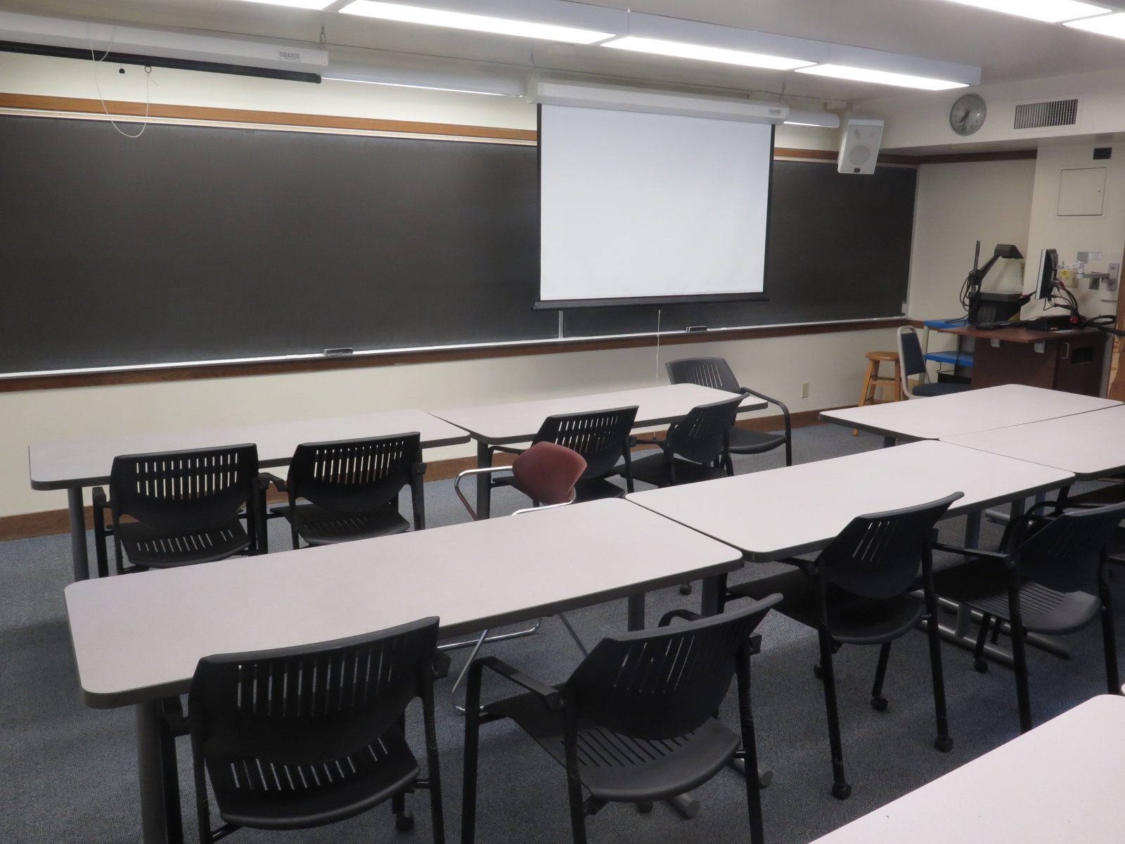View of BH 151 from back of room, Moveable tables and chairs. Chalkboard on the front wall, podium at the front of room
