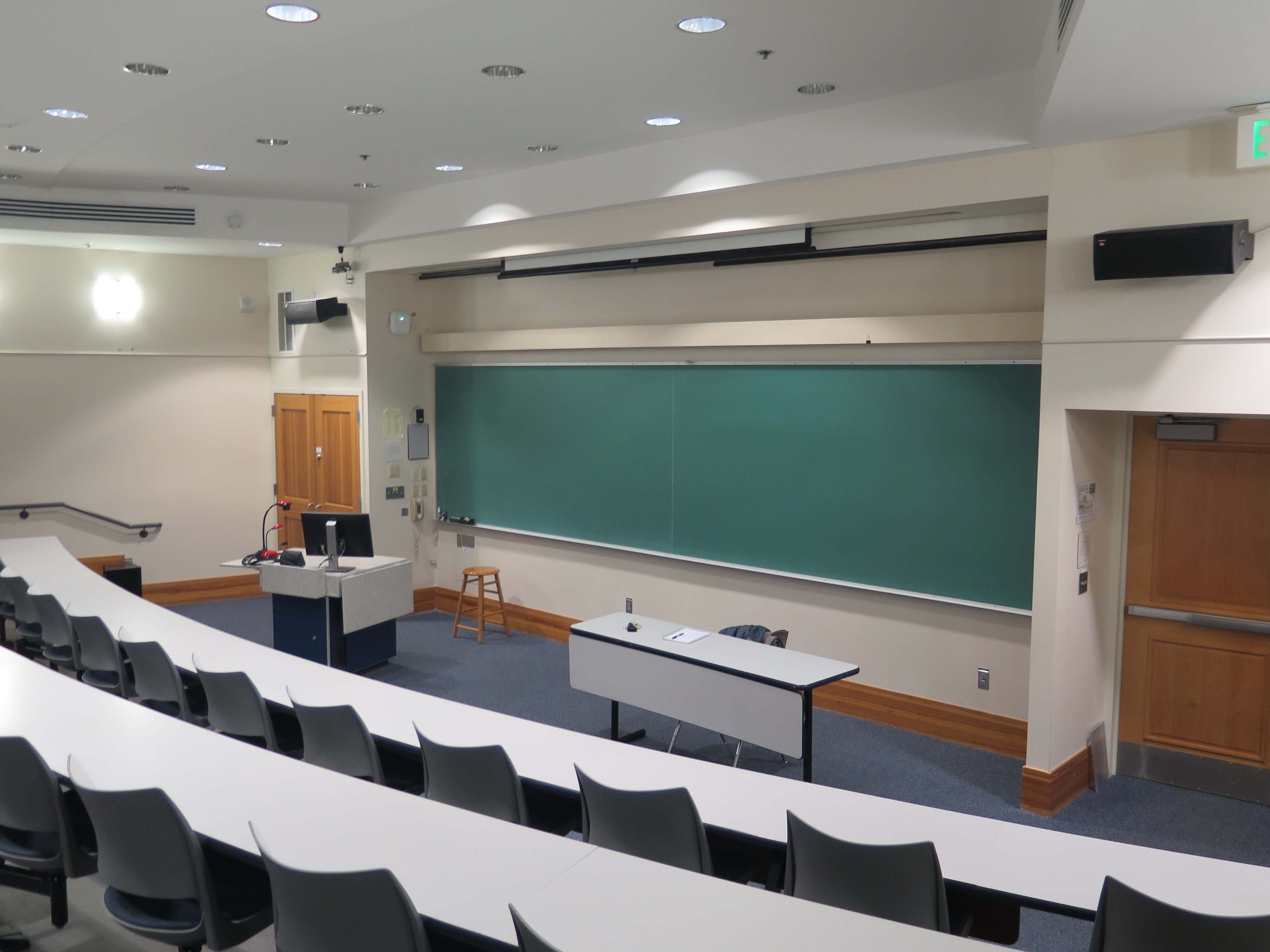 Room Consists of auditorium style, stationary tables and chairs, White board and podium are located at the front of the room.