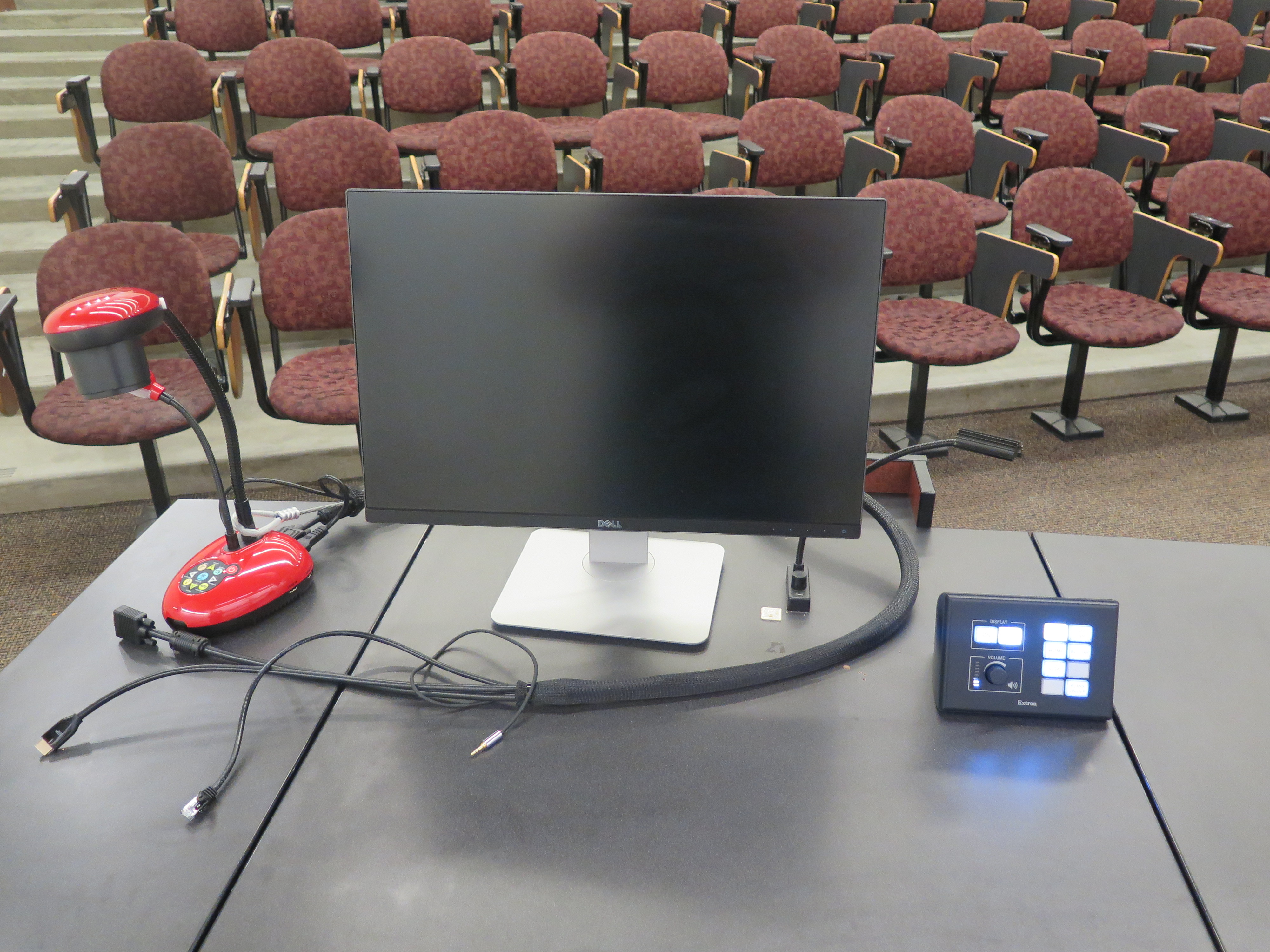 on top of podium is a dell computer monitor, AV push button controller, and lumins ladybug document camera