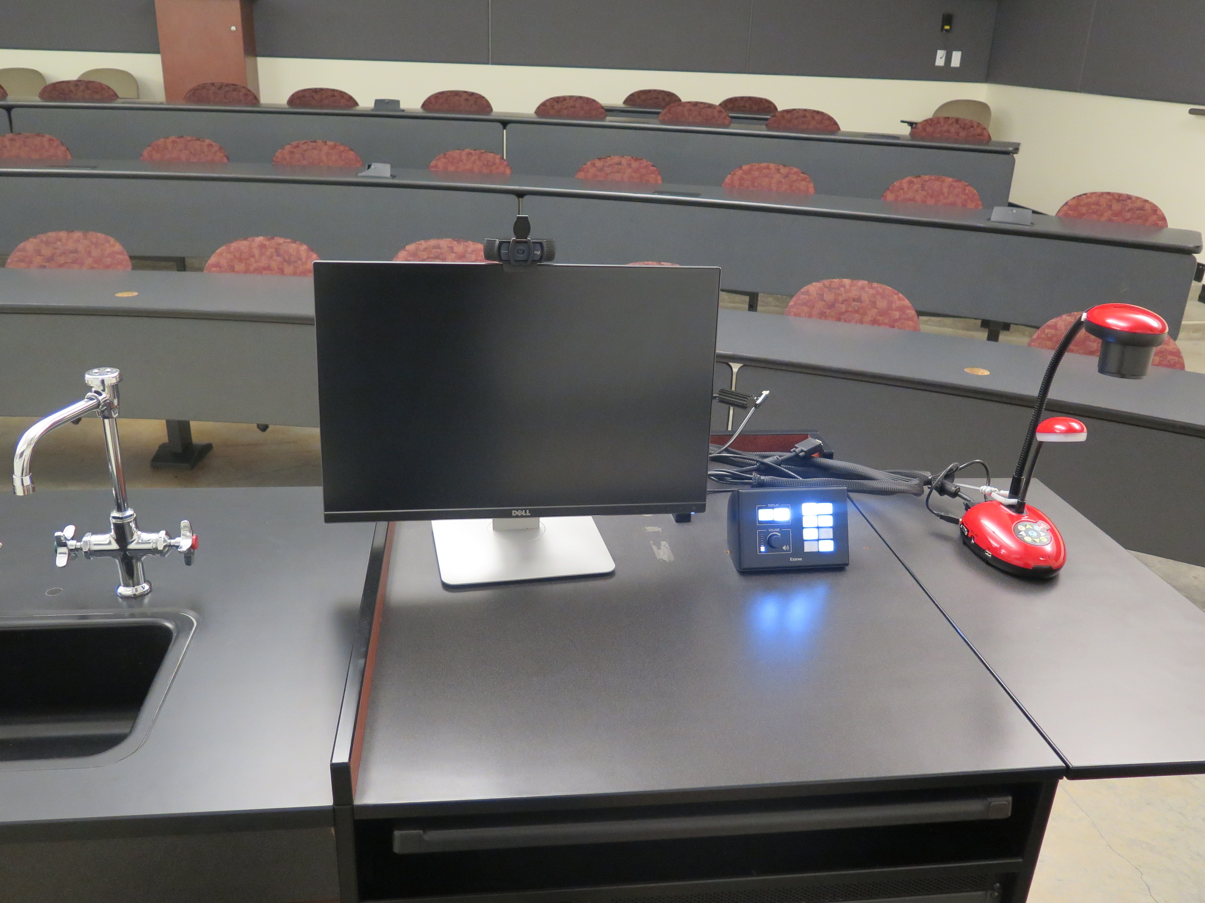 on top of podium is logitech 920 webcam, dell computer monitor, AV push button controller, and lumins ladybug document camera