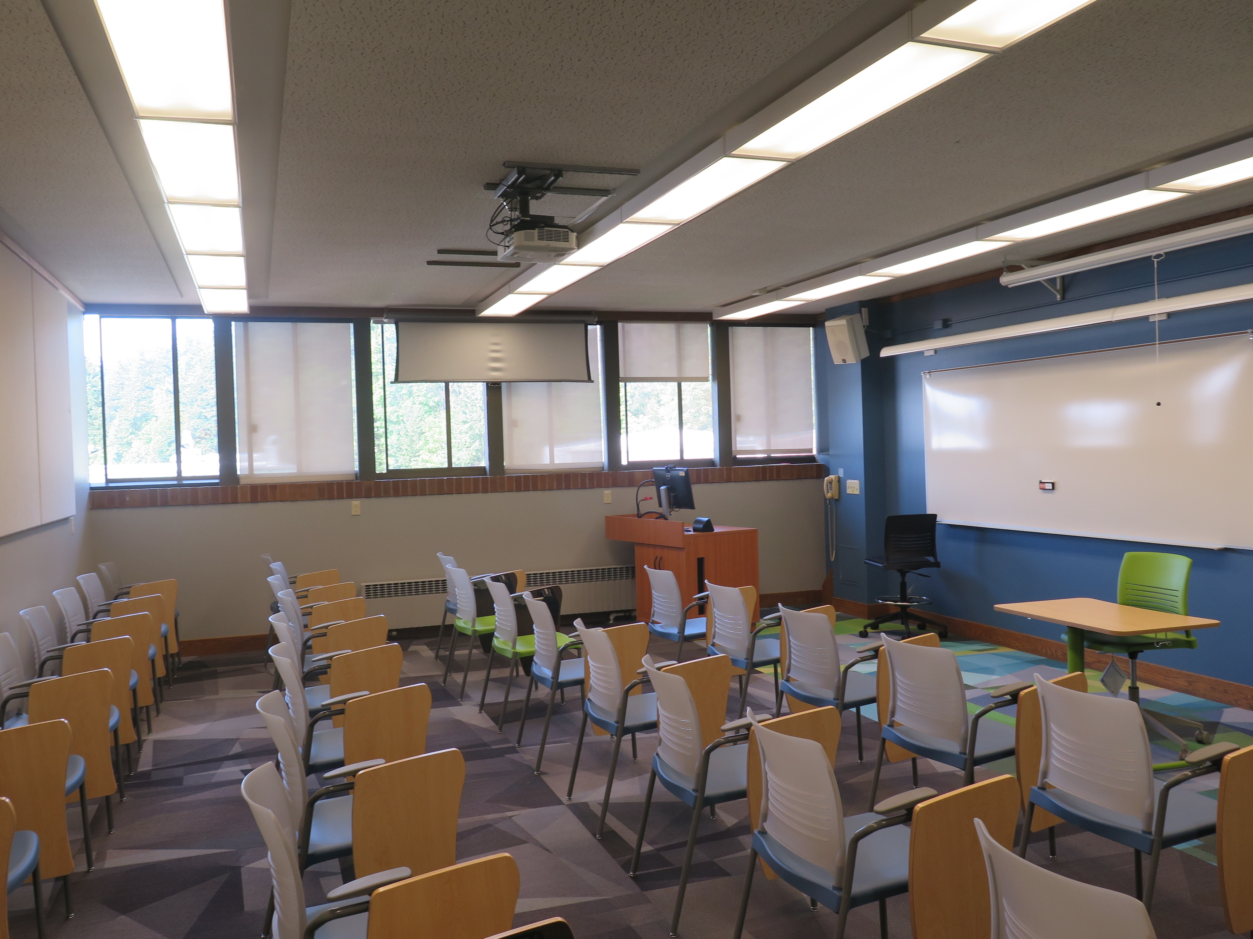 This room contains carpet floor, Moveable Tablet armchairs, whiteboard at the front of the room and a podium. 