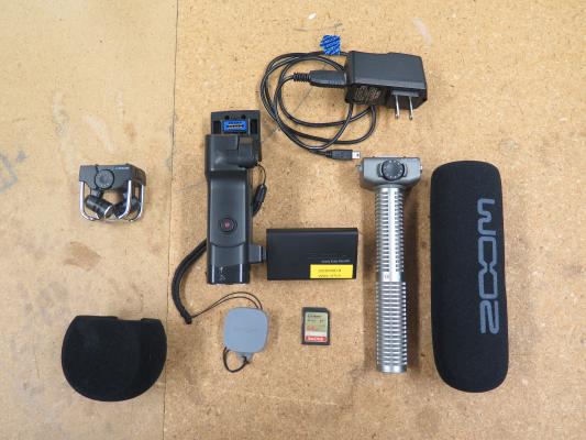 This image shows what comes in the bag. Includes Zoom Q8 recorder, Lens cap, Camera strap, two microphones that are interchangeable, SD card, microphone wind covers, and power cable.