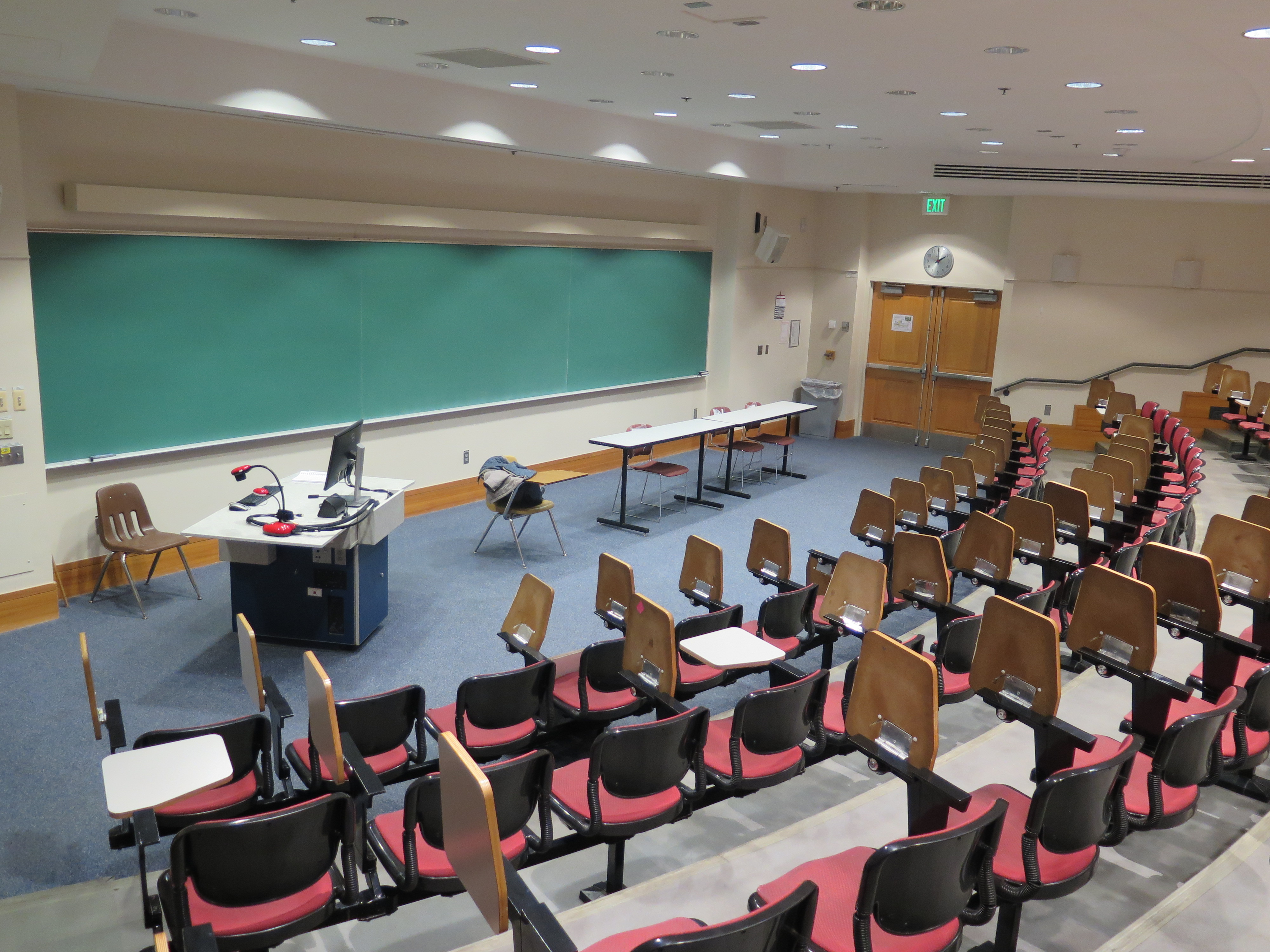 Room Consists of auditorium style, stationary tablet armchairs, White board and podium are located at the front of the room.